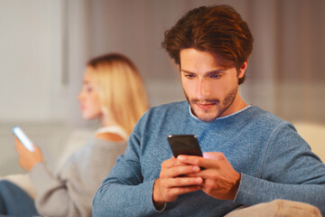 Infidelity. Cheating Husband Chatting On Mobile Phone Sitting Next To Wife On Sofa At Home. Selective Focus