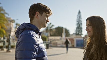 Poster - A man and woman stand on a sunlit urban street, exchanging smiles in a moment of connection.