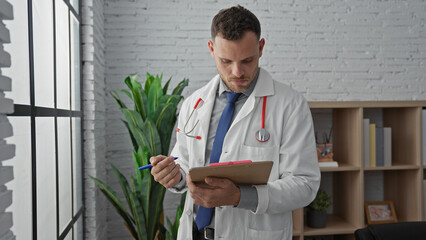 Wall Mural - A focused young man in a white lab coat intently writing on a clipboard in a bright clinic office.