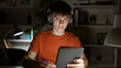 © Krakenimages.com - Focused teen boy studying late at night in a home interior, using a tablet and headphones.