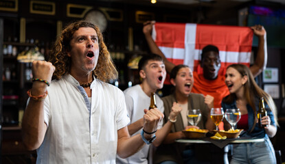 Poster - Excited multiracial soccer fans with flag of Switzerland celebrating victory of team with pint of beer and chips in the pub