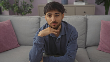 Canvas Print - A handsome bearded man sitting thoughtfully on a grey sofa in a modern apartment living room.