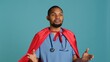 © DC Studio - Male nurse portraying superhero showing courage and strength fighting diseases, studio backdrop. Portrait of african american doctor posing as hero in costume, holding empowering speech, camera A