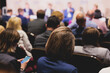 © tsuguliev - Female participants audience at the symposyum meeting, attendees in conference room hall listens to lecturer, group of women on a congress together listen to speaker on a stage at master-class