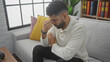 © Krakenimages.com - A pensive hispanic man with a beard sits worried in a modern living room.