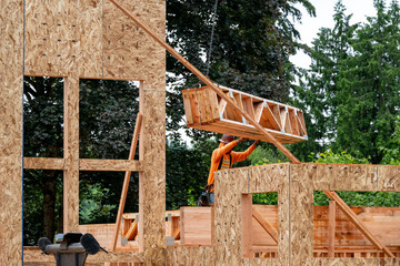 Wall Mural - Residential house construction, boom crane lifting lumber delivery, wood support truss beams, workman assisting in placement
