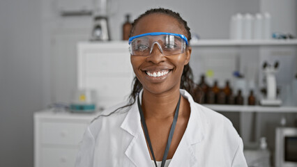 Sticker - African american woman scientist with curly hair wearing safety goggles and white lab coat in a laboratory setting