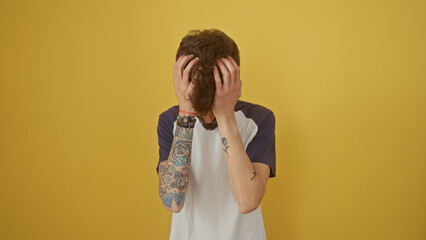 Poster - A distressed young man with tattoos covers his face against a plain yellow background.