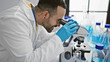 © Krakenimages.com - A young hispanic man with a beard works diligently in a lab, analyzing specimens under a microscope.