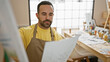 © Krakenimages.com - A focused man holding paper in an art studio examines his work with a contemplative expression.