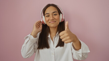 Sticker - Young attractive brunette woman with headphones giving a thumbs up over an isolated pink background, indicating positivity and confidence.