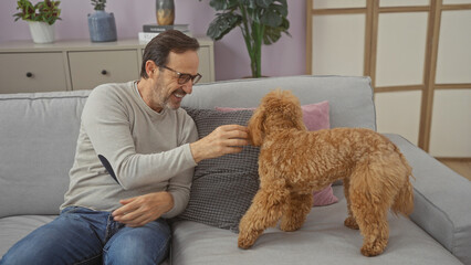 Canvas Print - A smiling hispanic man in casual clothing enjoys quality time with his poodle on a cozy sofa indoors.