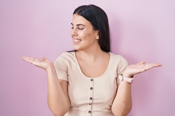 Sticker - Young hispanic woman standing over pink background smiling showing both hands open palms, presenting and advertising comparison and balance