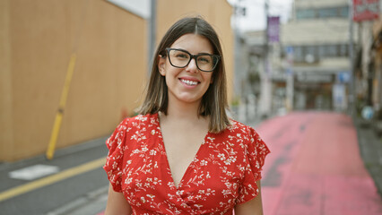 Poster - Laughing, carefree hispanic woman with beautiful smile and glasses, confidently posing on tokyo city's modern street, exuding a contagiously cheerful and positive aura