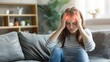 © LU - Woman feels dizzy and sits down on the couch. Young woman sitting on the sofa at home, feeling pain and a spinning sensation in her head. Concept of headache, vertigo, health problem, brain tumor