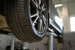 © sofiko14 - Close-up of tire on vehicle lift in auto repair shop showing car maintenance, inspection, tire check, and automotive detail. Industrial background with focus on tread pattern.