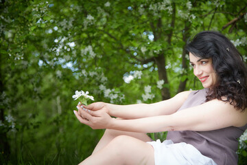 Joyous brunette woman near Blossoms of apple tree in a Spring Garden outdoors. Concept of face and body care. The scent of perfume and tenderness