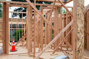 Wall Mural - New house construction in residential neighborhood, job site detail looking through window opening to subfloor, wood framed walls, and orange safety cone
