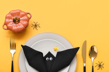 Festive table setting with Halloween bat, pumpkin and spiders on yellow background