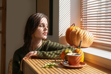 Wall Mural - Young woman near window at home on autumn day