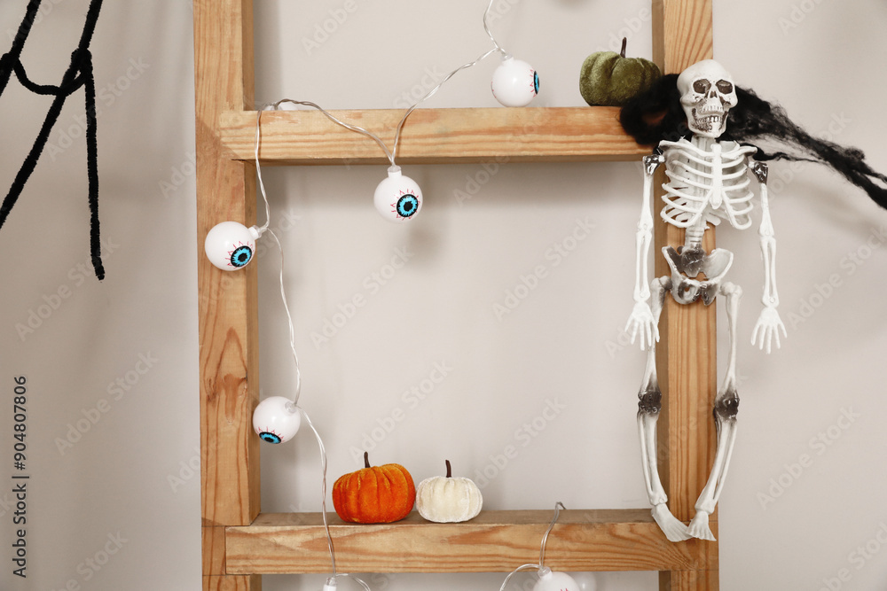 Wooden ladder with Halloween decor near light wall