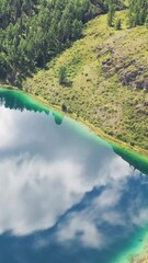 Wall Mural - Vertical aerial video of Altai mountain lake Uchkol with reflection of blue sky and clouds. Ulagan Plateau.