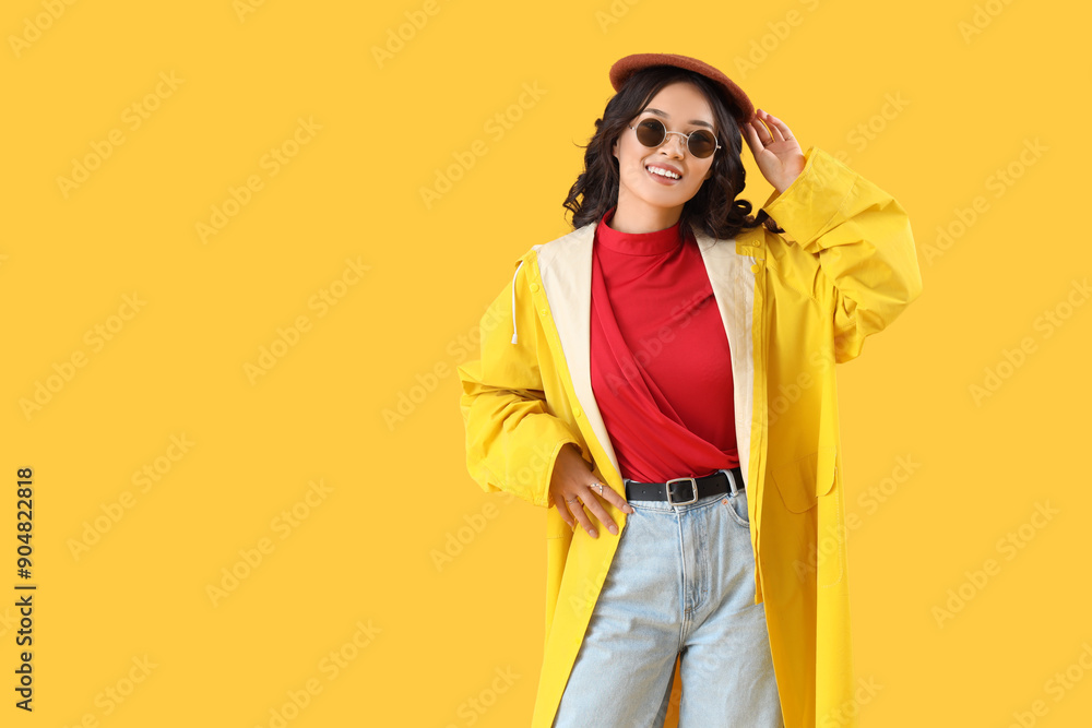 Stylish young Asian woman in fall clothes on yellow background