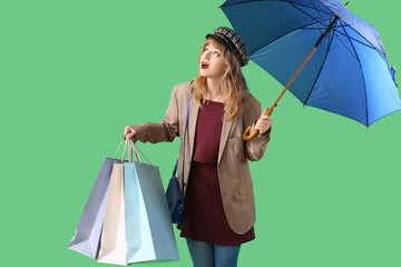 Poster - Stylish young woman in fall clothes with umbrella and shopping bags on green background