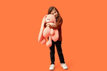 Wall Mural - Cute stylish little girl with bunny toy on orange background