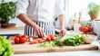 © Meow Creations - Chef preparing a healthy vegetarian meal, chopping fresh vegetables on a wooden cutting board in a bright kitchen.