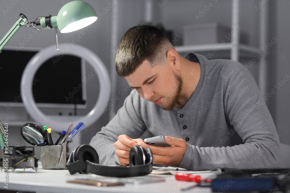 Male technician repairing mobile phone at table in service center