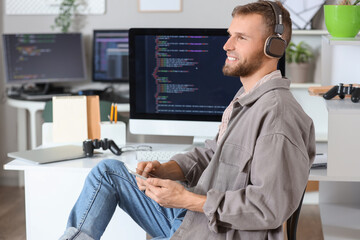 young bearded programmer with headphones and tablet computer working at table in office
