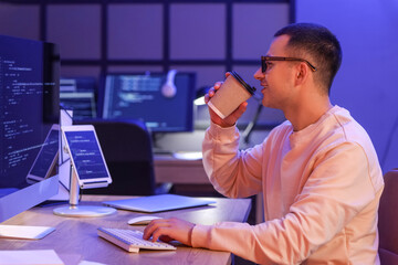 Wall Mural - Handsome programmer drinking coffee in office at night