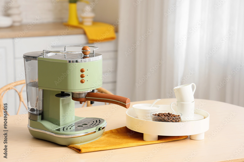 Modern coffee machine with cups, sugar and beans on table in kitchen