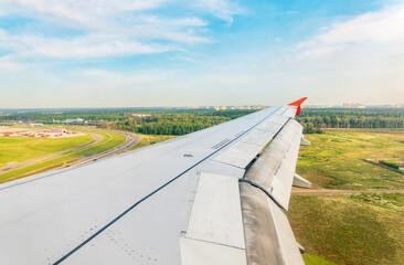 Wall Mural - View of airplane wing, blue skies and green land during landing. Airplane window view.