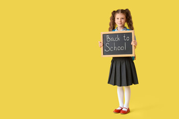 Wall Mural - Little girl holding chalkboard with text BACK TO SCHOOL on yellow background