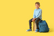 © Pixel-Shot - Little schoolboy with backpack sitting on books against yellow background