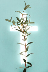 Wall Mural - Shining cross and eucalyptus branch on turquoise background. Religion of Christianity