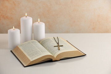 Cross with chain, burning candles and Bible on white table. Religion of Christianity