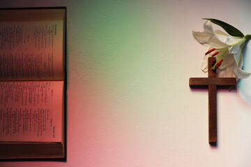 Wooden cross, Bible and lily flower on textured table in color lights, flat lay with space for text. Religion of Christianity