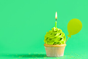 Wall Mural - Sweet Birthday cupcake with burning candle on green background