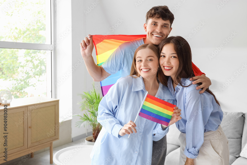 Young man with two women at LGBT flags at home. Polyamory concept