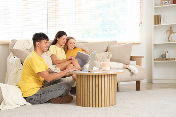 Canvas Print - Young man using laptop with two women reading magazine at home. Polyamory concept