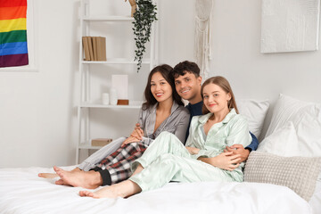 Wall Mural - Young man with two women hugging in bedroom. Polyamory concept