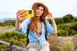 © maxbelchenko - Female travel blogger admires of nature view and shoots video blog on phone. Caucasian woman traveler using mobile phone taking selfie while solo travel in summer sunny day.