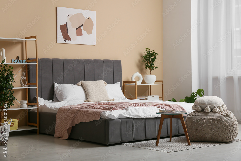 Interior of stylish bedroom with shelf units, pouf and table