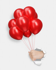 Childrens hand holding red shiny balloons through the hole in white paper