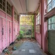 © Colin - Abandoned school hallway with pink lockers, glass windows, and overgrown plants in postmodern architecture.