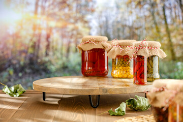 Sticker - Autumn pickles of vegetables in glass jars on autumn table with an empty space for products. In the background, an autumn forest trees with yellow and orange leaves.