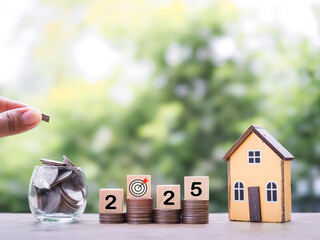 Poster - Miniature house, Wooden blocks with the number 2025 and stack of coins. The concept of saving money for house, Property investment, House mortgage, Real estate in year 2025